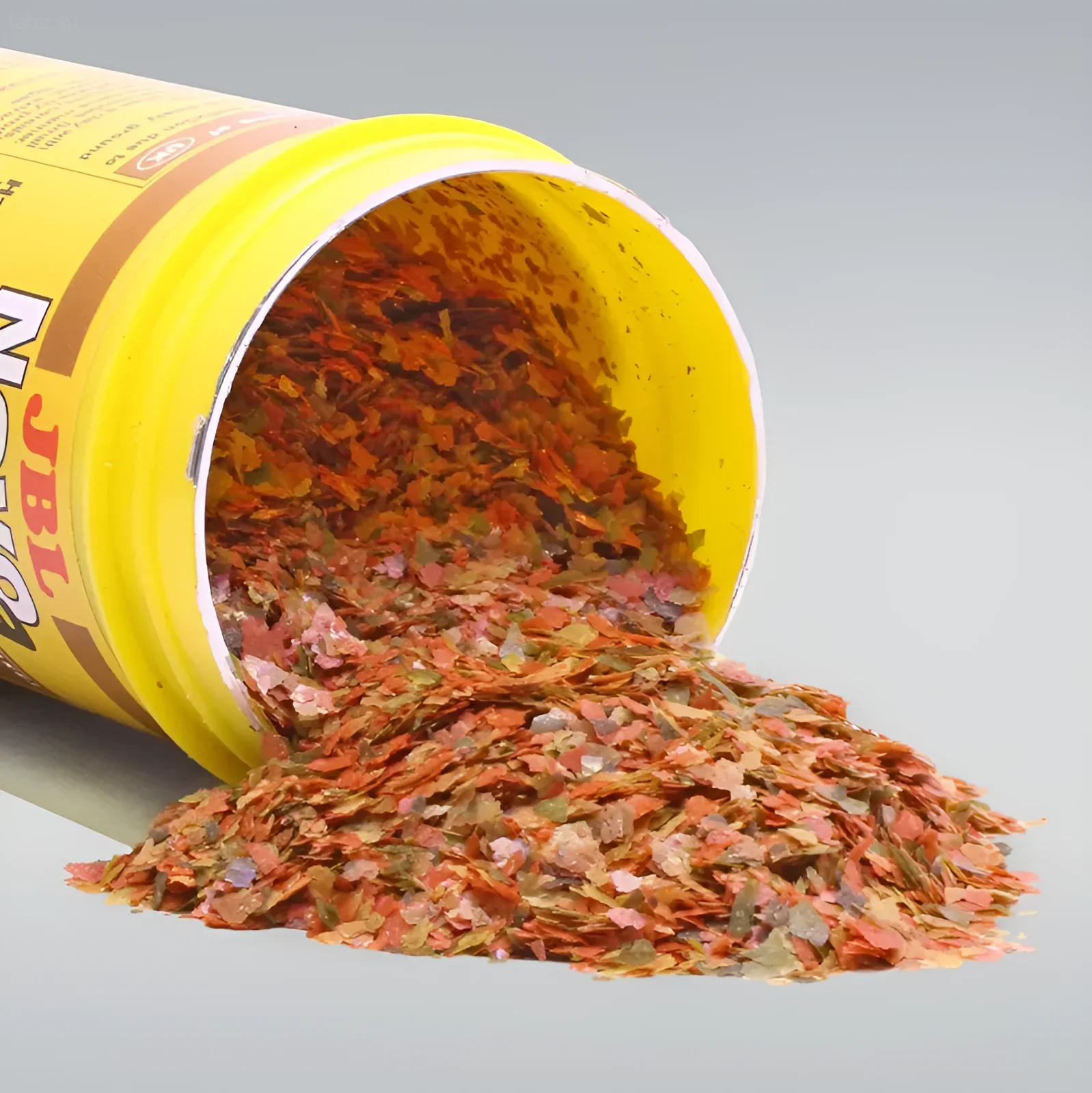 Фотография рассыпанных хлопьев для аквариумных рыб из желтой банки. Подчеркивает разнообразие цветов и текстур корма.